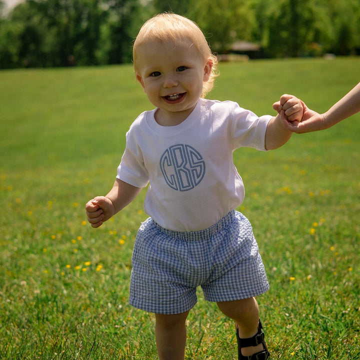 Smiling baby in monogrammed shirt and shorts.